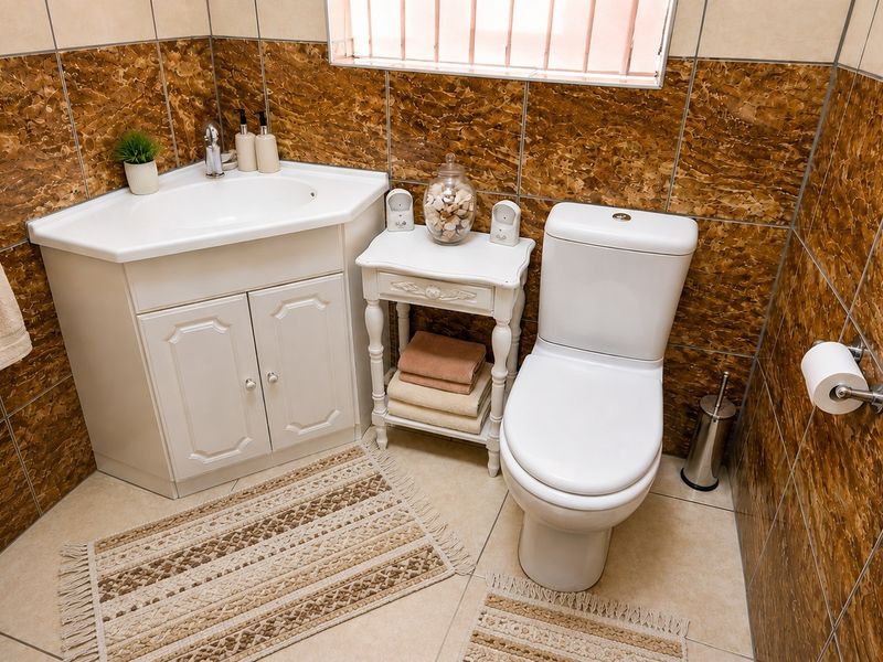 A compact bathroom featuring a corner vanity unit, ceramic basin, and toilet, finished with decorative brown wall tiles and neutral floor tiles.