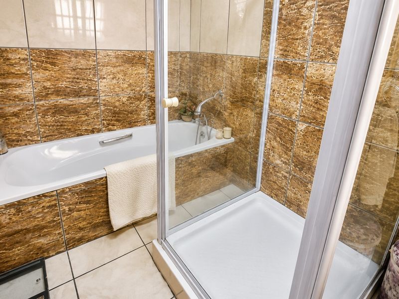 A functional bathroom featuring a built-in bathtub and a separate glass-enclosed shower, finished with decorative brown marble-effect wall tiling.