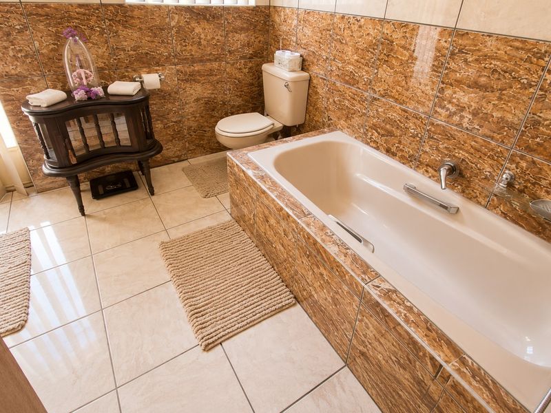 A bathroom featuring a built-in bathtub with chrome fixtures, a toilet, and full-height marble-effect wall tiling with neutral floor tiles.