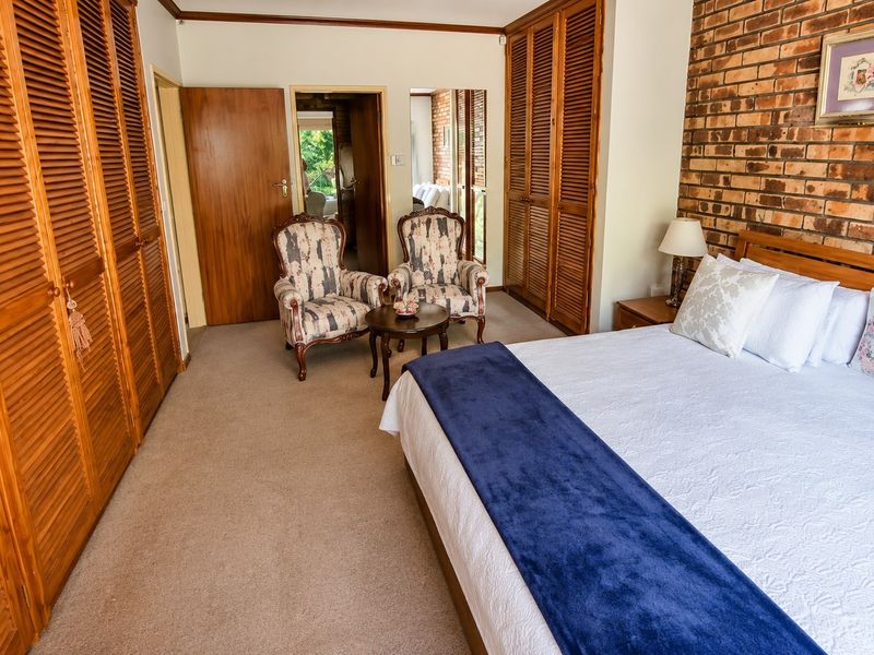 Spacious bedroom featuring built-in louvered wardrobes, an exposed brick feature wall, and neutral carpeting, offering a warm and traditional aesthetic.