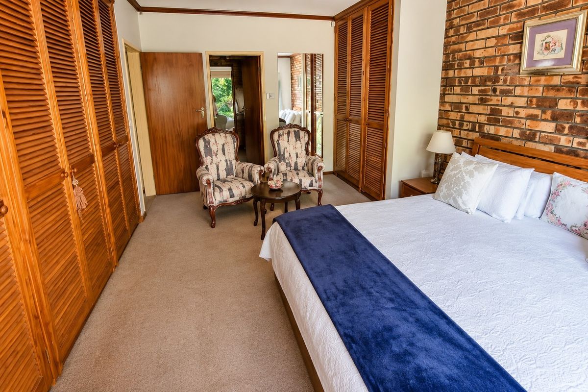 Spacious bedroom featuring built-in louvered wardrobes, an exposed brick feature wall, and neutral carpeting, offering a warm and traditional aesthetic.