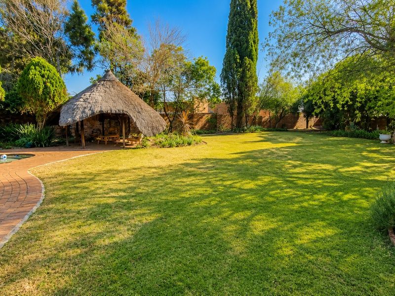 Spacious landscaped garden featuring a large lawn, a traditional thatched lapa, brick-paved pathways, and a swimming pool area.