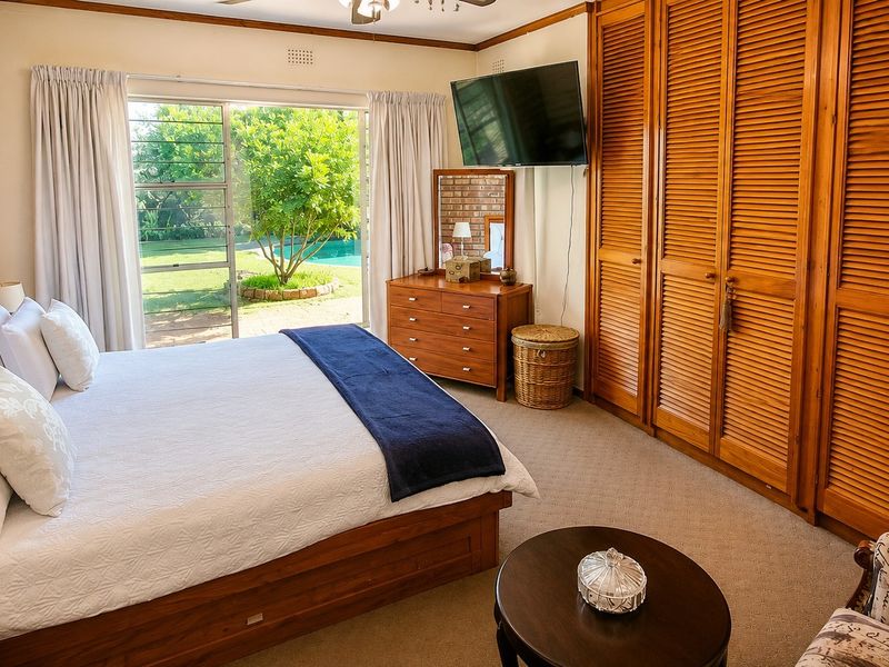 Spacious bedroom featuring built-in wooden louvered wardrobes, an exposed brick feature wall, and sliding glass doors providing direct access to the garden and pool area.
