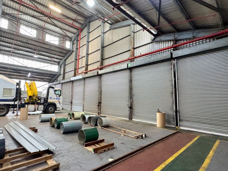 Spacious industrial warehouse featuring high ceilings, exposed steel trusses, multiple roller shutter doors, and durable concrete flooring suitable for logistics or manufacturing operations.