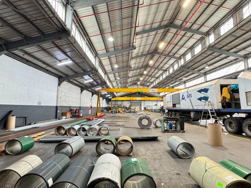 Spacious industrial warehouse featuring high ceilings, exposed steel trusses, overhead gantry crane, and durable concrete flooring, suitable for manufacturing or logistics operations.