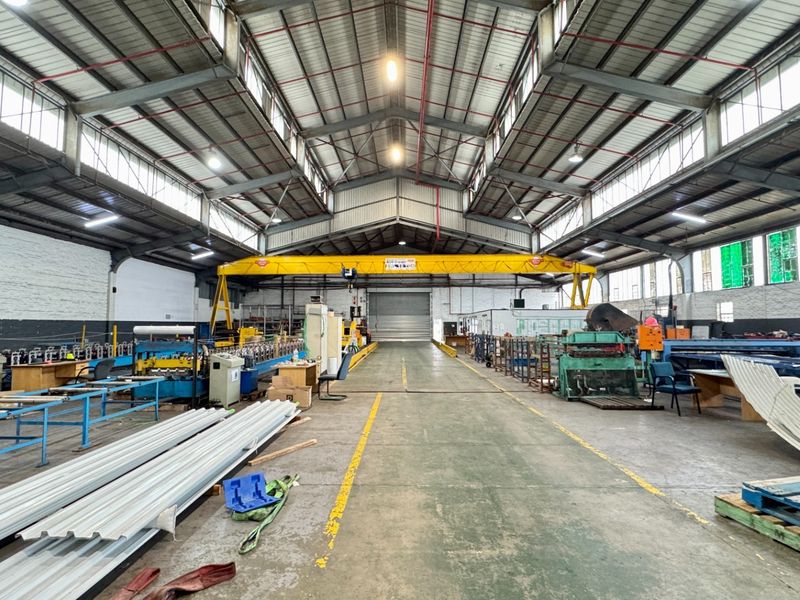 Spacious industrial warehouse facility featuring high ceilings, an overhead gantry crane, concrete flooring, and natural light through clerestory windows.