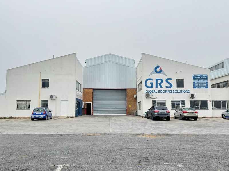 Front elevation of an industrial warehouse facility featuring a large roller shutter door, metal cladding, and paved concrete apron.