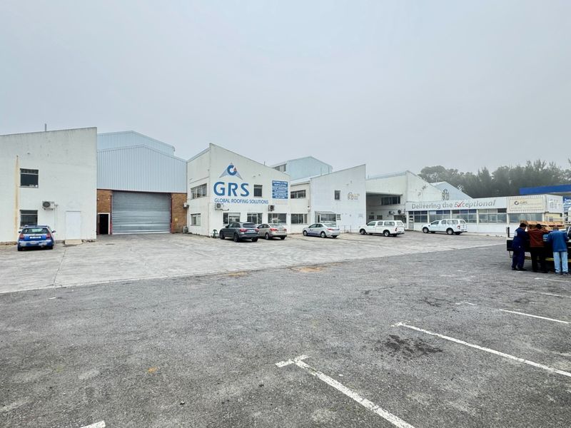 Front elevation of an industrial warehouse facility featuring a large roller shutter door, concrete yard area, and dedicated parking bays.