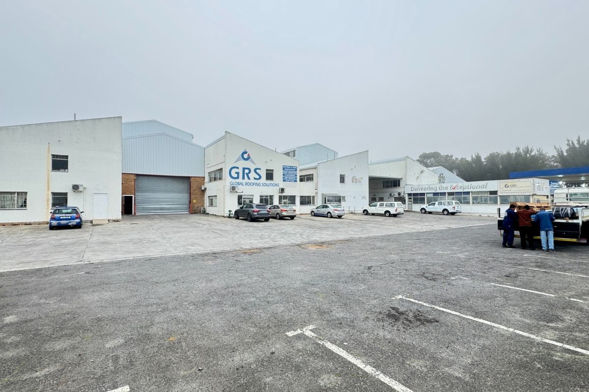 Front elevation of an industrial warehouse facility featuring a large roller shutter door, concrete yard area, and dedicated parking bays.
