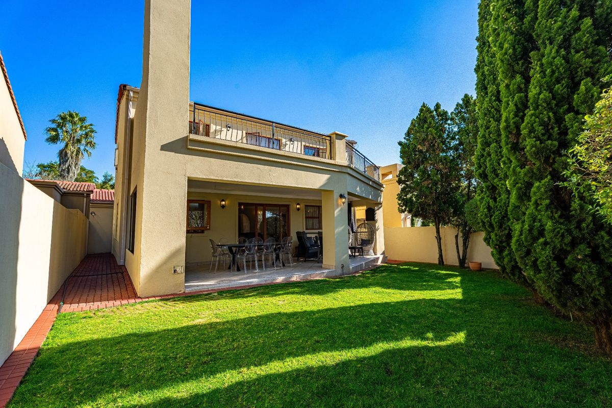 Rear view of the townhouse featuring a covered patio, an upper-level balcony with wrought iron railings, a chimney, and a well-maintained garden.