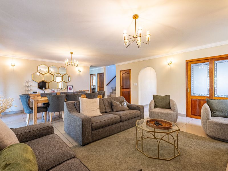 Spacious open-plan living and dining area featuring tiled floors, coved cornicing, elegant chandeliers, and classic timber doors leading to other parts of the home.