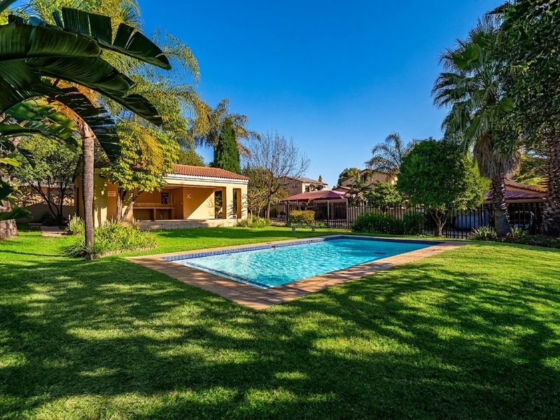 A well-maintained backyard featuring a swimming pool with tiled surround, a lush lawn, and a covered patio area with a built-in braai.
