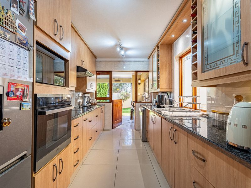 A well-maintained galley-style kitchen featuring light wood cabinetry, granite countertops, built-in oven, and tiled flooring, with direct access to the rear patio area.
