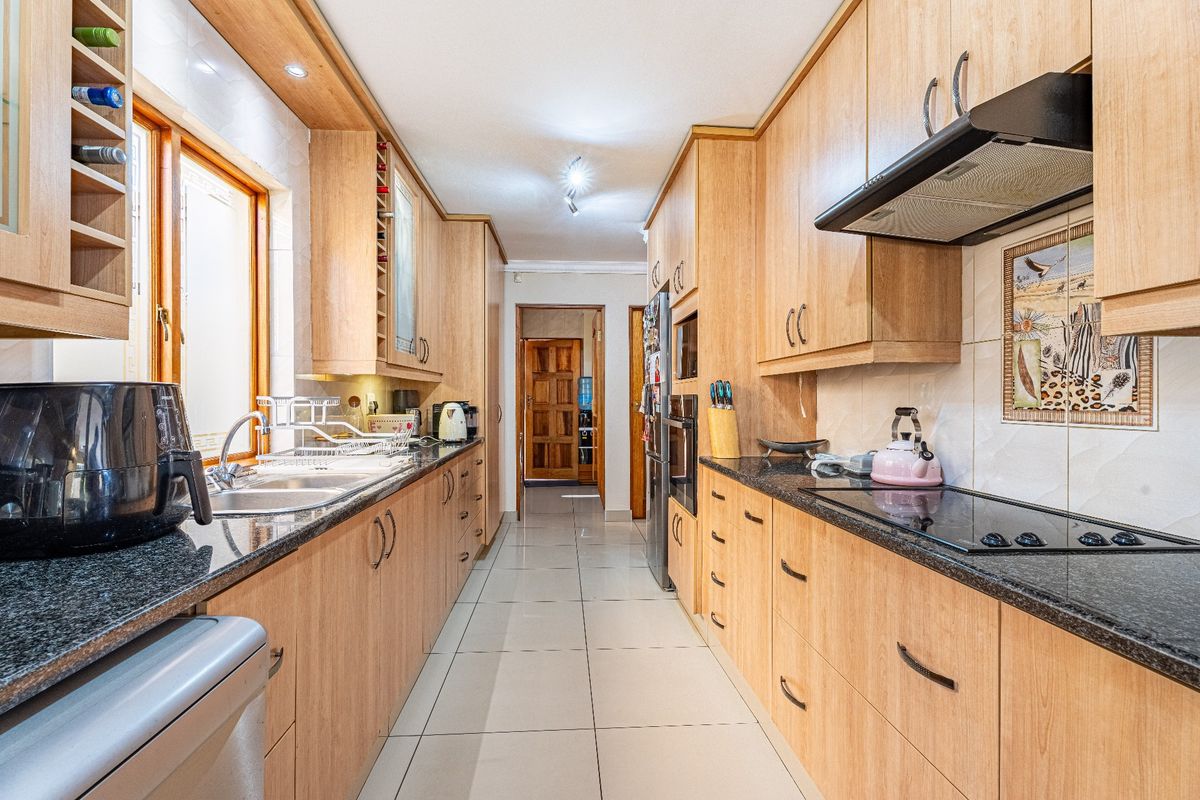 A functional galley-style kitchen featuring light wood cabinetry, granite countertops, integrated appliances, and tiled flooring.
