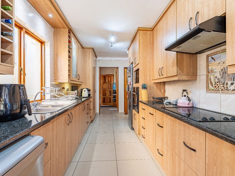 A functional galley-style kitchen featuring light wood cabinetry, granite countertops, integrated appliances, and tiled flooring.