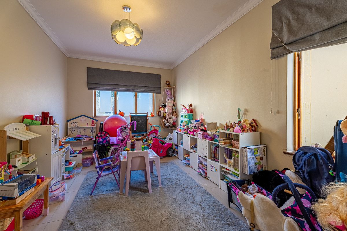 A bedroom featuring tiled flooring, crown molding, and dual windows with roman blinds, currently utilized as a play area.