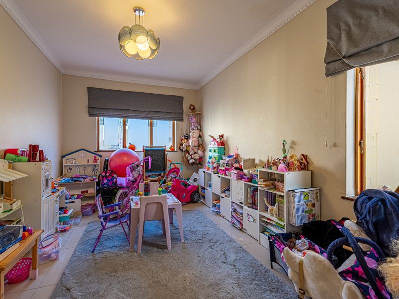 A bedroom featuring tiled flooring, crown molding, and dual windows with roman blinds, currently utilized as a play area.