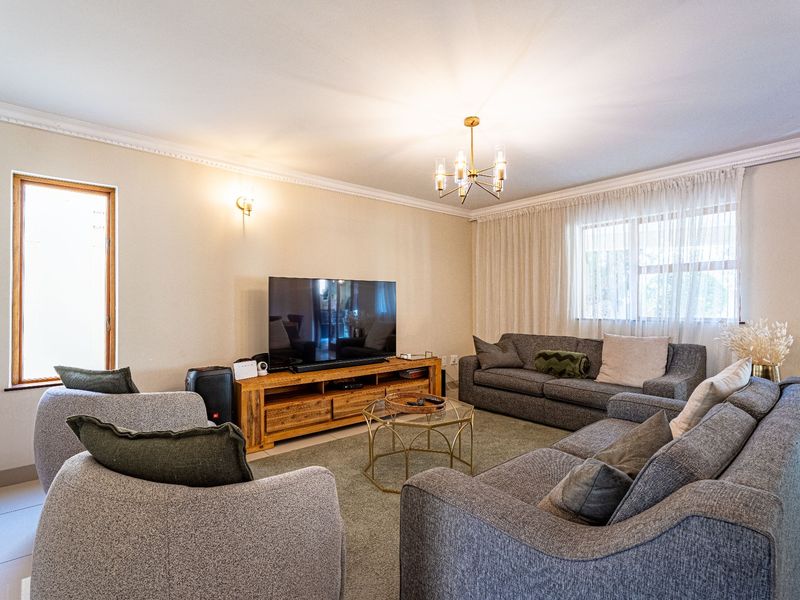 A well-maintained living room featuring crown molding, tiled flooring, and a modern chandelier, creating a comfortable and inviting space.