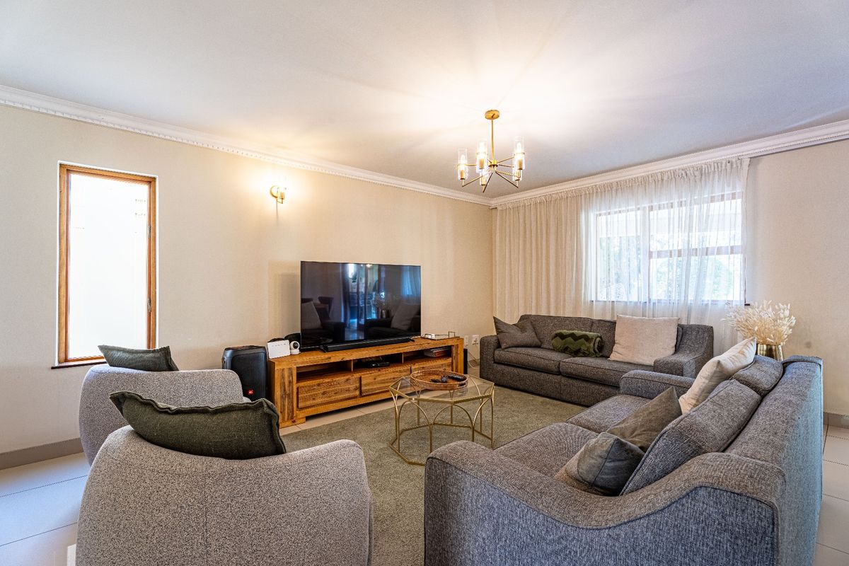 A well-maintained living room featuring crown molding, tiled flooring, and a modern chandelier, creating a comfortable and inviting space.