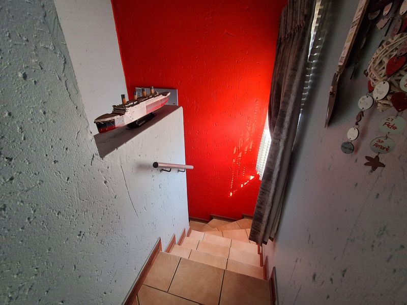 A narrow staircase featuring tiled steps, a wall-mounted handrail, and a bold red accent wall.