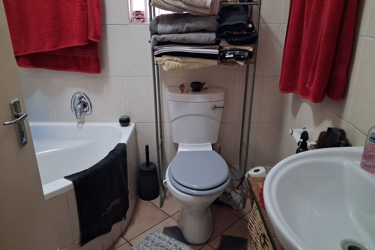 A functional bathroom featuring a built-in bathtub, pedestal basin, and toilet with neutral ceramic wall and floor tiling.
