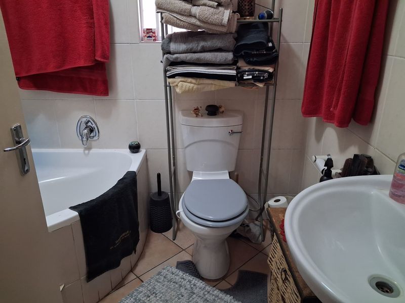A functional bathroom featuring a built-in bathtub, pedestal basin, and toilet with neutral ceramic wall and floor tiling.