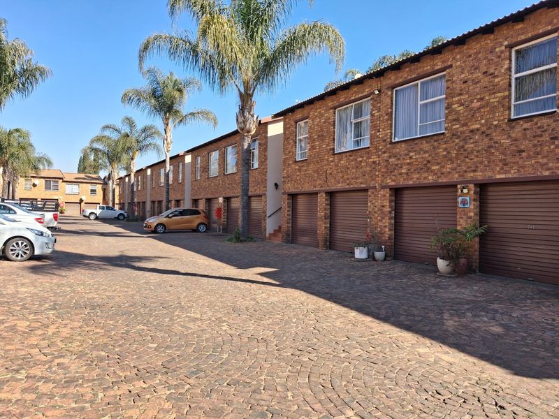 Exterior view of a townhouse complex featuring a paved driveway, multiple roll-up garage doors, and classic brick facade construction.