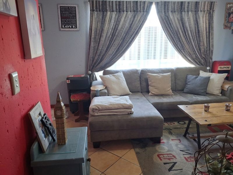 A living room featuring tiled flooring and a large window with curtain treatments, providing a functional space for relaxation.
