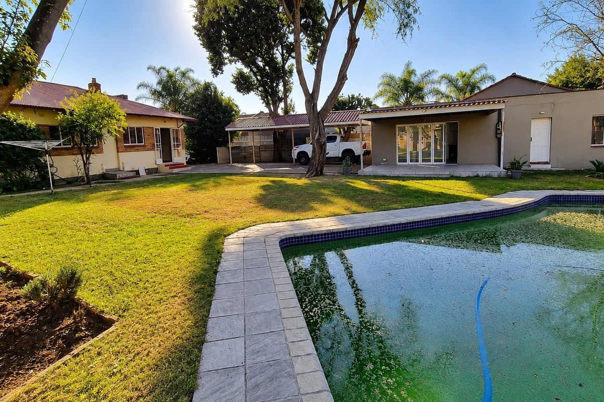 Spacious rear garden featuring a swimming pool, paved patio area, and a carport, offering potential for outdoor entertainment and landscaping improvements.