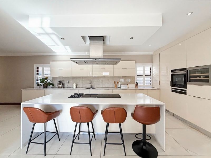 Modern, high-end kitchen featuring a large central island with integrated hob, sleek cabinetry, built-in appliances, and recessed lighting in a bright, open space.