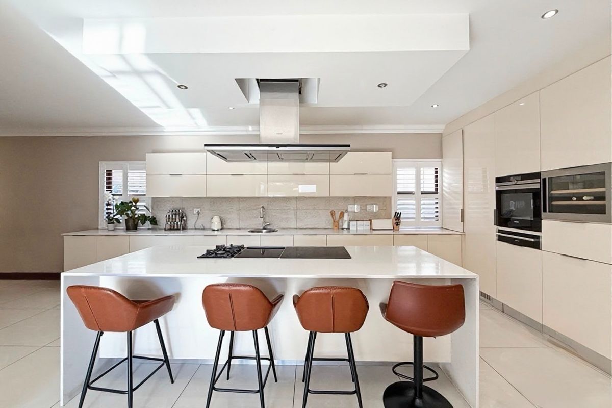 Modern, high-end kitchen featuring a large central island with integrated hob, sleek cabinetry, built-in appliances, and recessed lighting in a bright, open space.