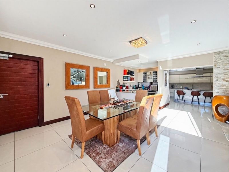 Spacious open-plan dining and kitchen area featuring modern porcelain tiling, recessed lighting, and a contemporary kitchen with a stone island and built-in cabinetry.
