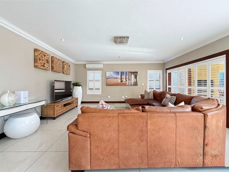 Spacious living room featuring tiled flooring, recessed downlights, crown molding, and plantation shutters, providing a bright and comfortable atmosphere.