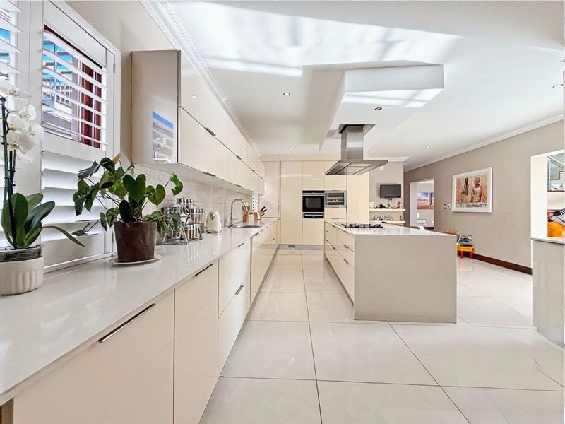 Modern, spacious kitchen featuring high-gloss cabinetry, a large central island with a gas hob, integrated appliances, and sleek quartz countertops.