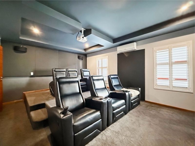 Dedicated home cinema room featuring tiered seating, acoustic wall treatments, a ceiling-mounted projector, and plantation shutters for light control.