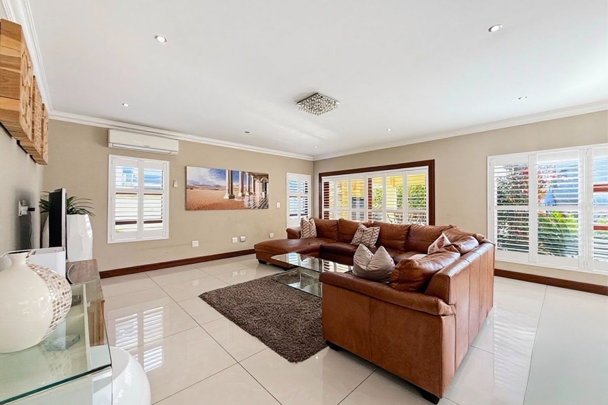 Spacious living room featuring polished porcelain floor tiles, plantation shutters, and a split-system air conditioner, offering a bright and well-maintained living environment.