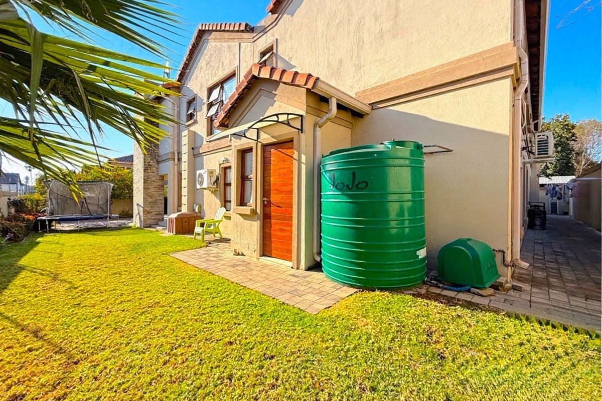 Rear exterior view of the property featuring a landscaped garden, paved pathway, and a large green water storage tank.