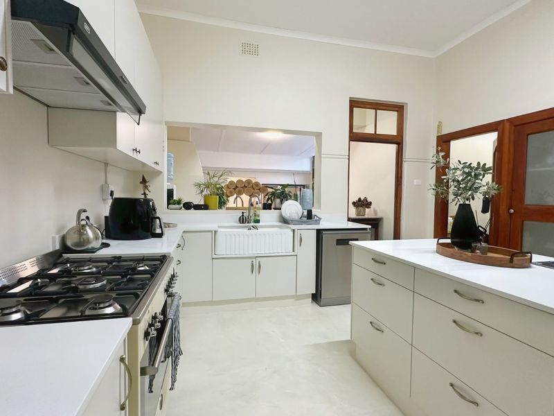 A well-maintained kitchen featuring a gas cooktop, extractor fan, apron front sink, and a central island with stone countertops and ample cabinetry.