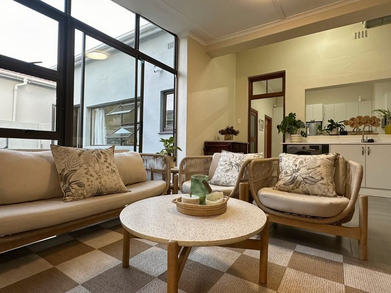Bright open-plan living area featuring large windows, tiled flooring, and a functional kitchen space with built-in cabinetry.