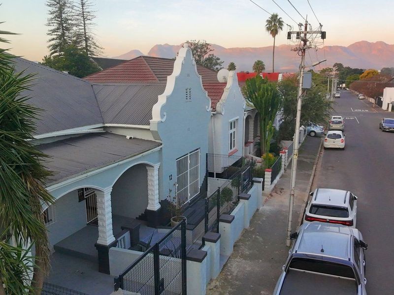 Elevated street view of a charming house featuring a distinctive gabled facade, covered porch, and secure perimeter fencing in a residential neighborhood.