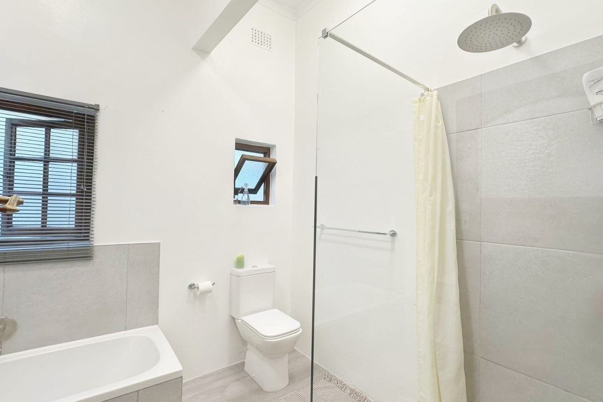 Modern bathroom featuring a walk-in shower with a rain shower head, a built-in bathtub, and neutral tiled finishes.