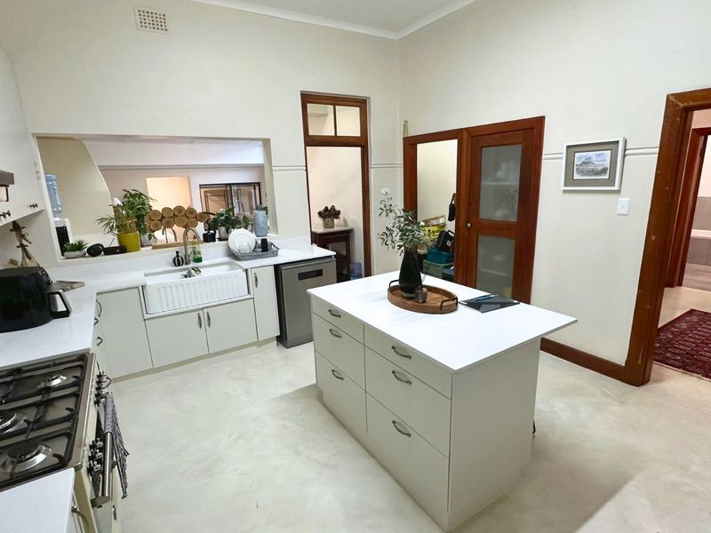A well-maintained kitchen featuring a central island, farmhouse sink, gas cooktop, and classic timber door frames, offering a bright and functional workspace.