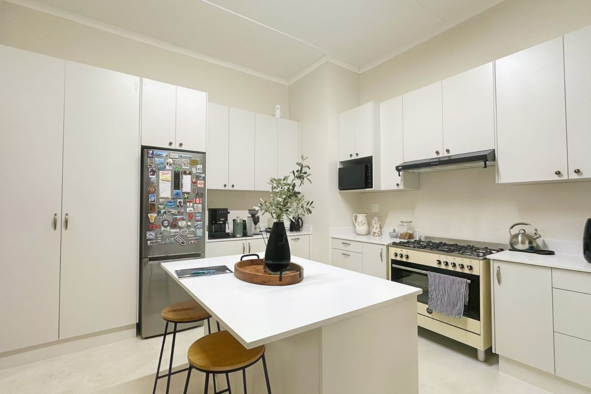A clean, modern kitchen featuring white cabinetry, a central island, and a gas stove with an integrated extractor fan.