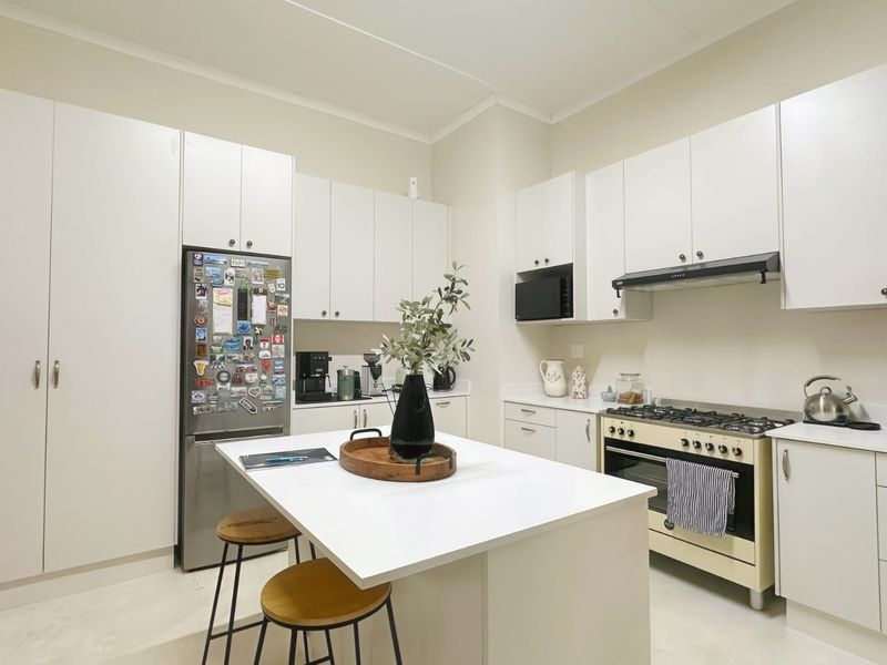 A clean, modern kitchen featuring white cabinetry, a central island, and a gas stove with an integrated extractor fan.