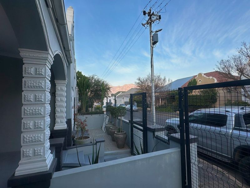 Front elevation of the property featuring a covered porch with decorative columns, secure perimeter fencing, and a paved entrance area.