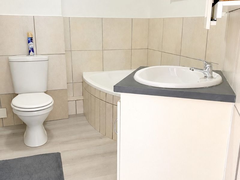 A functional bathroom featuring a corner bathtub, a vanity unit with a washbasin, and neutral wall tiling.