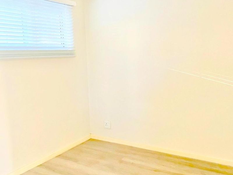 A clean, empty bedroom featuring light-toned laminate flooring, neutral walls, and fitted venetian blinds.