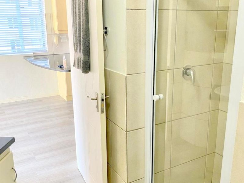 A functional bathroom featuring a glass-enclosed shower with tiled finishes, adjacent to an open-plan living and kitchen area.