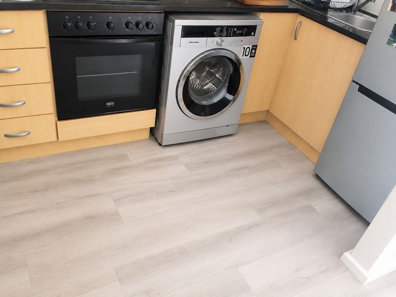 A functional kitchen area featuring light wood-finish cabinetry, a built-in oven, and modern light-toned laminate flooring.