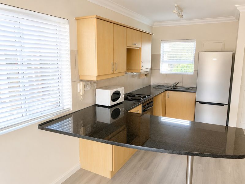 A functional kitchen featuring light wood cabinetry, black granite countertops, an electric hob, and an integrated sink with natural light from dual windows.